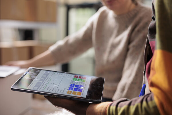 Stockroom workers analyzing online customers orders on digital device, preparing packages for shipping. Diverse employees working at merchandise logistics in warehouse. Close up shot
